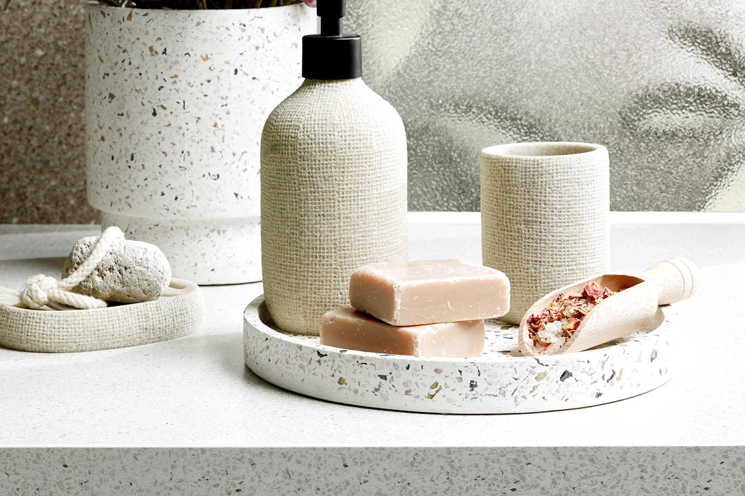 Terrazzo-style bathroom tray with soap bars, dispenser, and bath accessories on a white vanity countertop