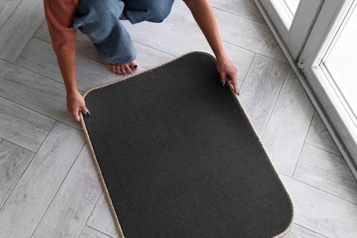Hands placing a black anti-slip floor mat on a light grey tile surface, ideal for hotel entrances or guest bathrooms