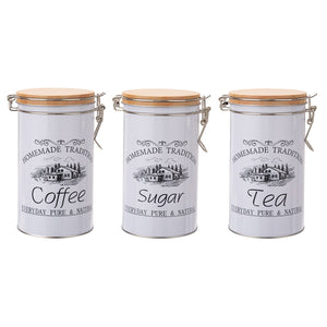 Black and white iron canisters labeled ‘Sugar,’ ‘Coffee,’ and ‘Tea’ arranged on a rustic wooden countertop
